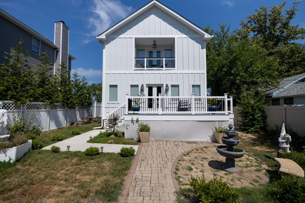 Modern white two-story house with paved walkway and decorative fountain in landscaped yard.