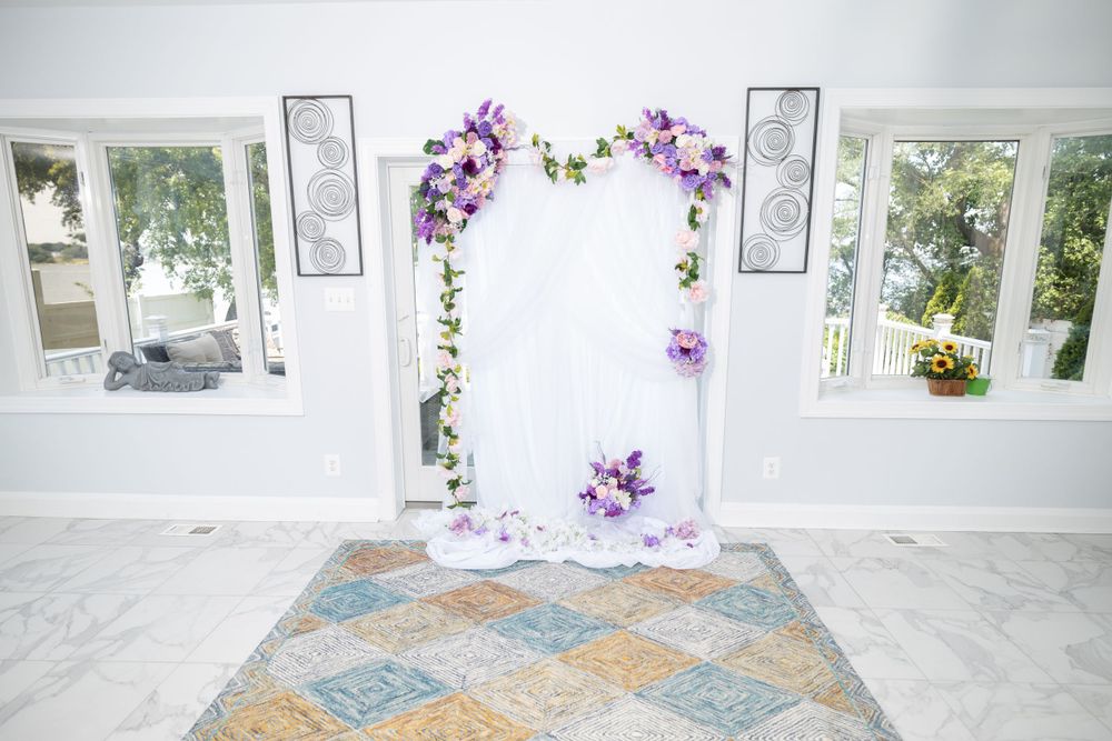 Wedding ceremony venue with floral arch, white walls and elegant patterned floor.