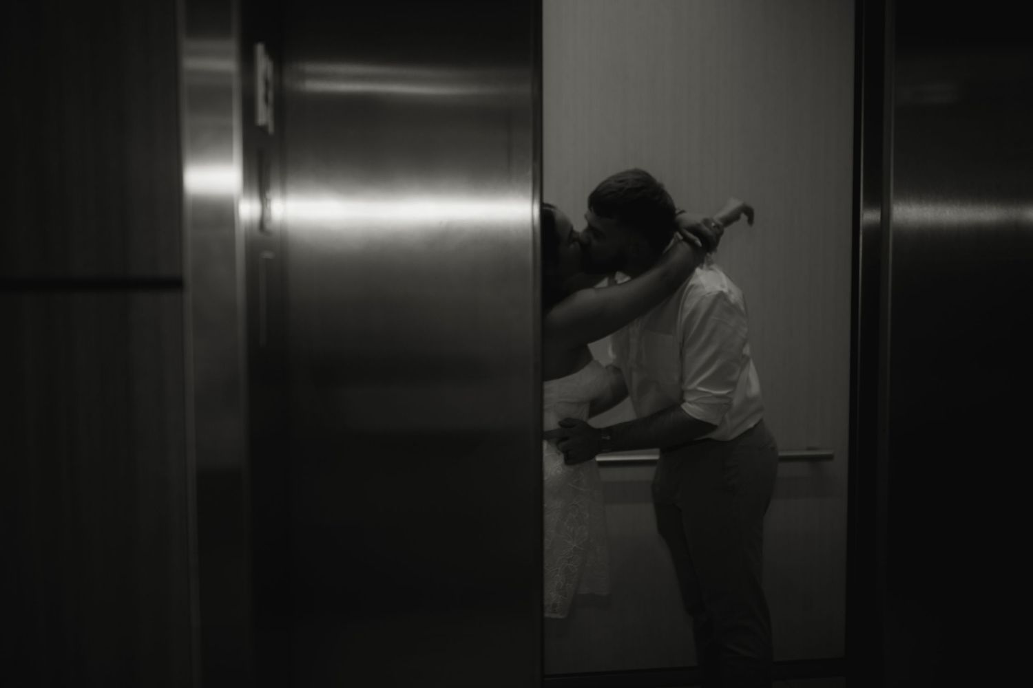 Black and white image showing a silhouette of a person in a hallway with metal elevator doors.