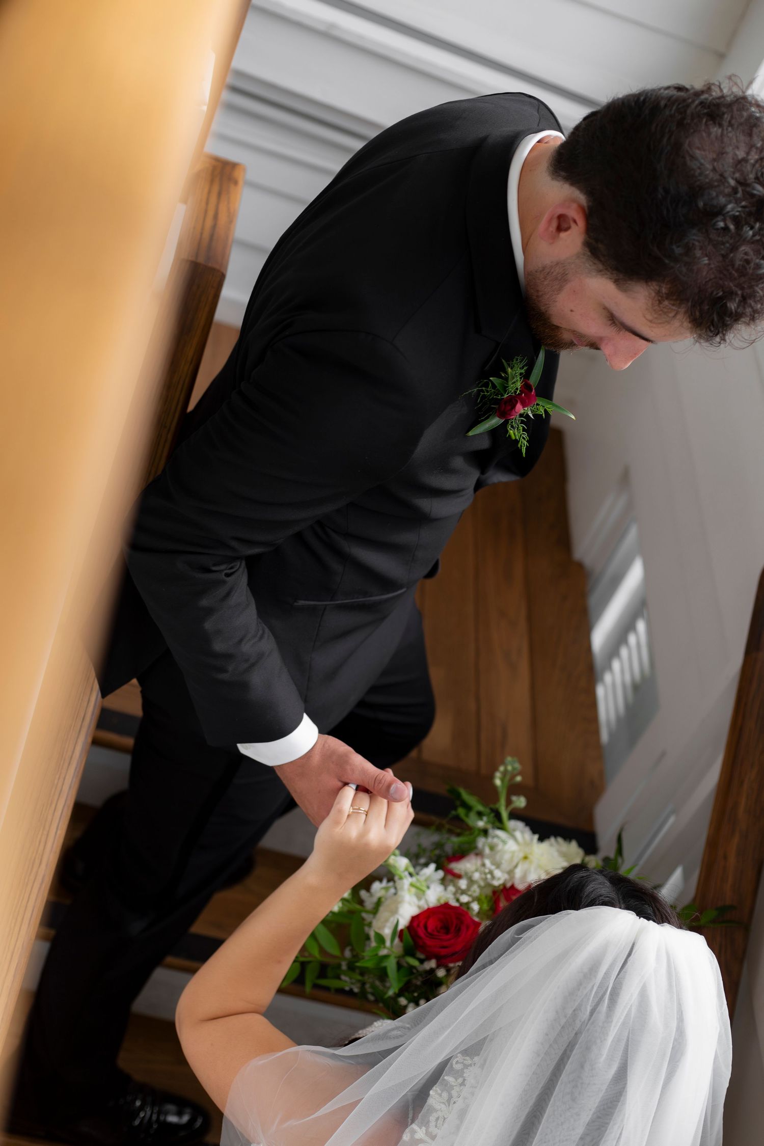 A person in a black suit and someone in a white veil hold hands during an intimate wedding moment.