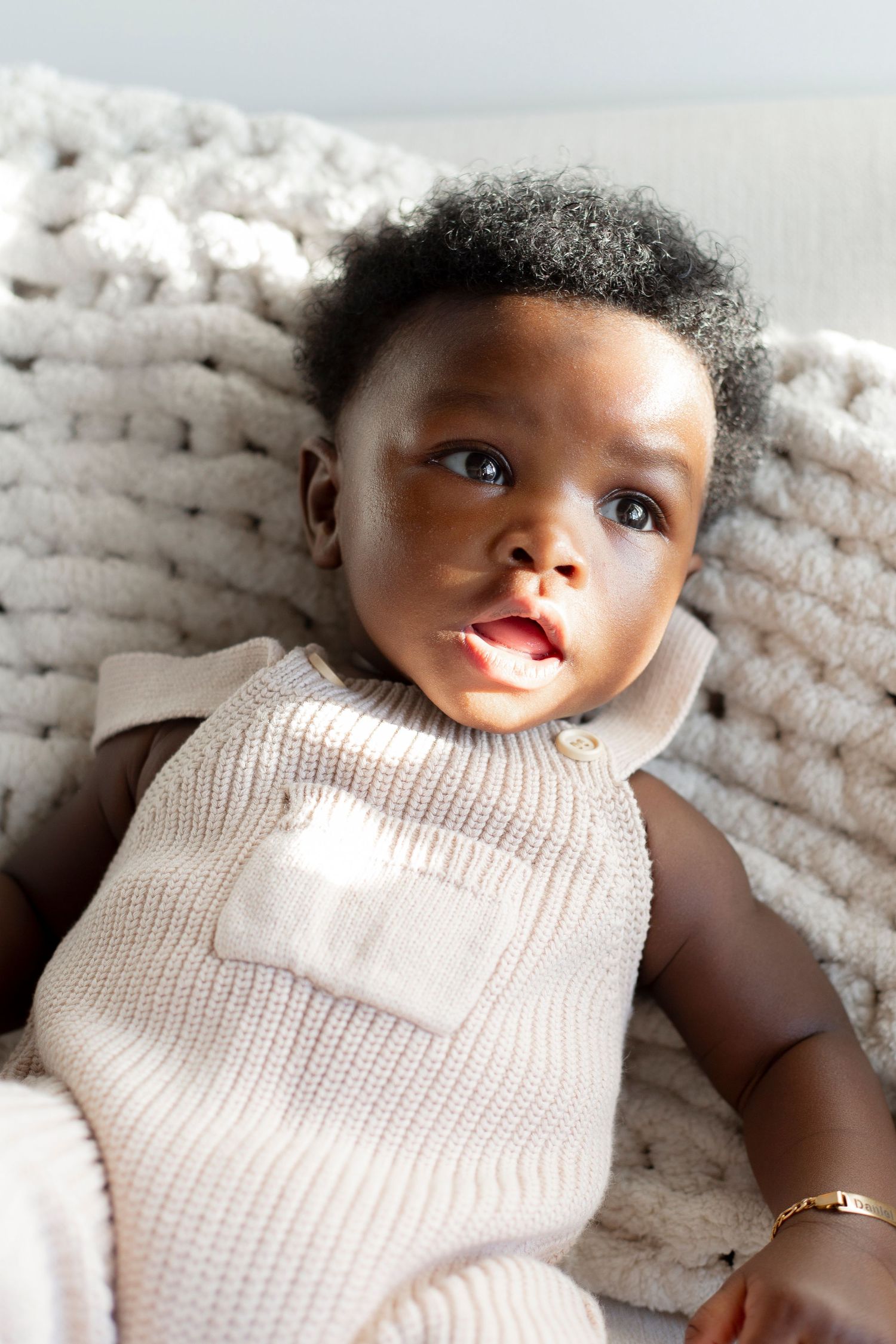 Young child wearing a cream knit sweater relaxes against a chunky knit blanket in a soft portrait setting.