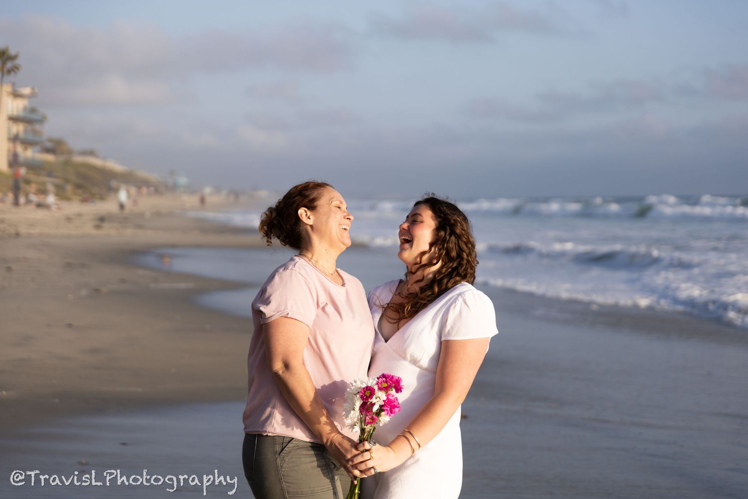 Happy couple sharing laughter on beach with ocean waves in background.