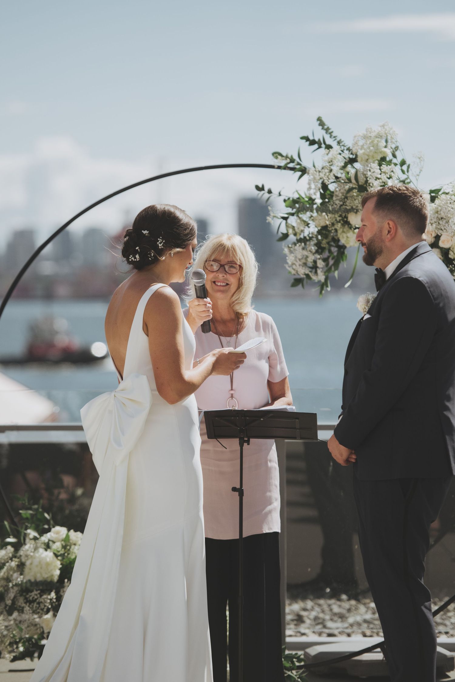 Outdoor waterfront wedding ceremony with floral arch and intimate exchange of vows.