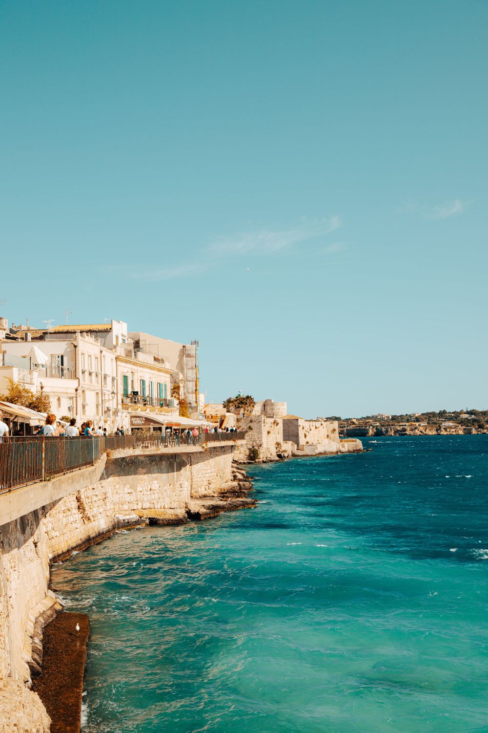 Stunning turquoise coastline with historic stone buildings along the Mediterranean waterfront in Sicily, Italy.