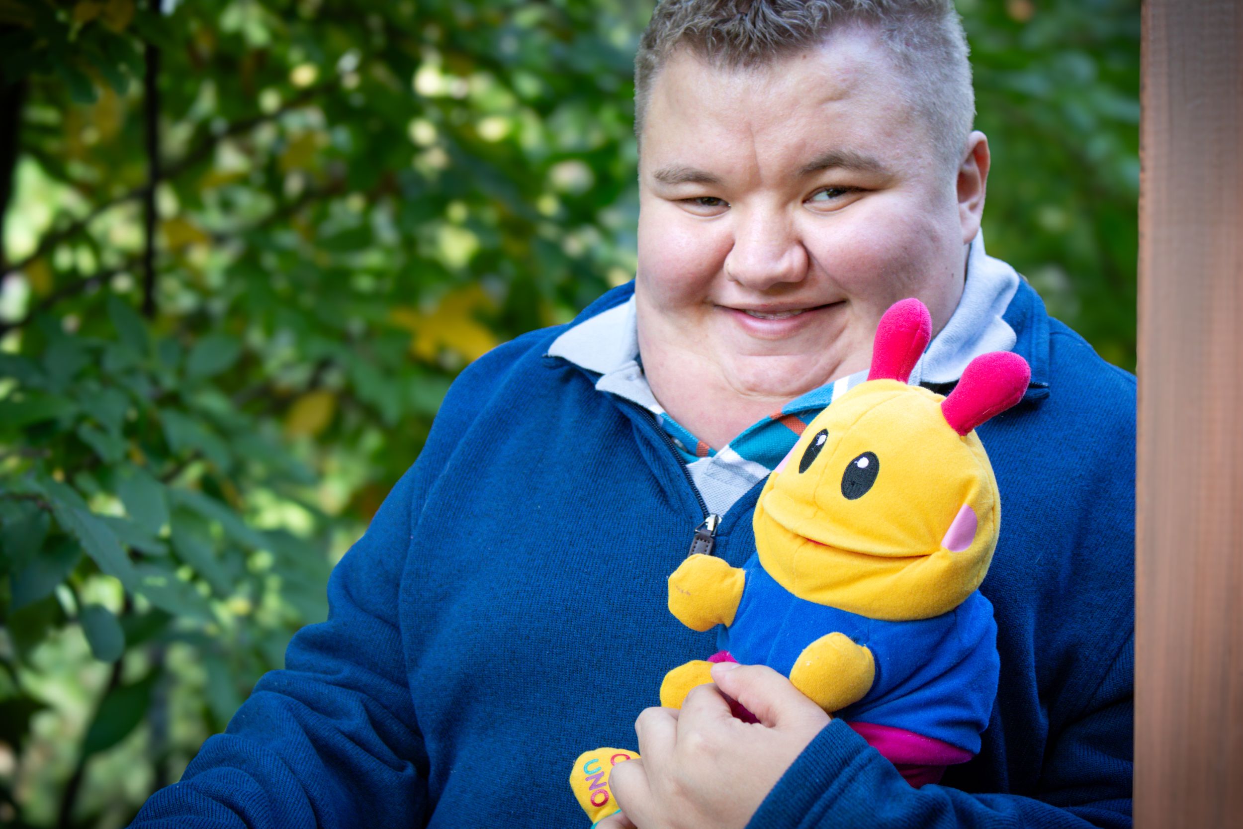 Senior portrait of a boy holding his favorite toy standing in the doorway of an outdoor building.