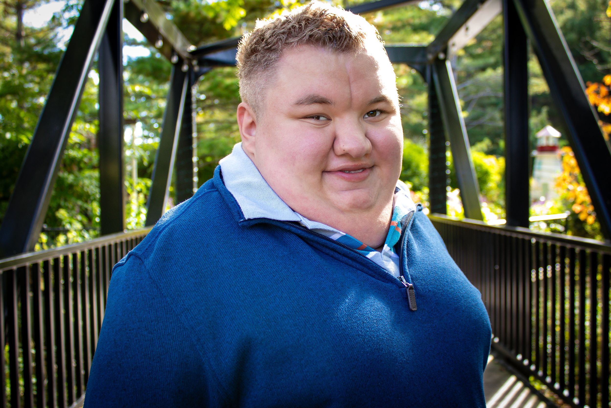 Senior portrait of a boy on a bridge backlit by the sun surrounded by trees and strong architecture.