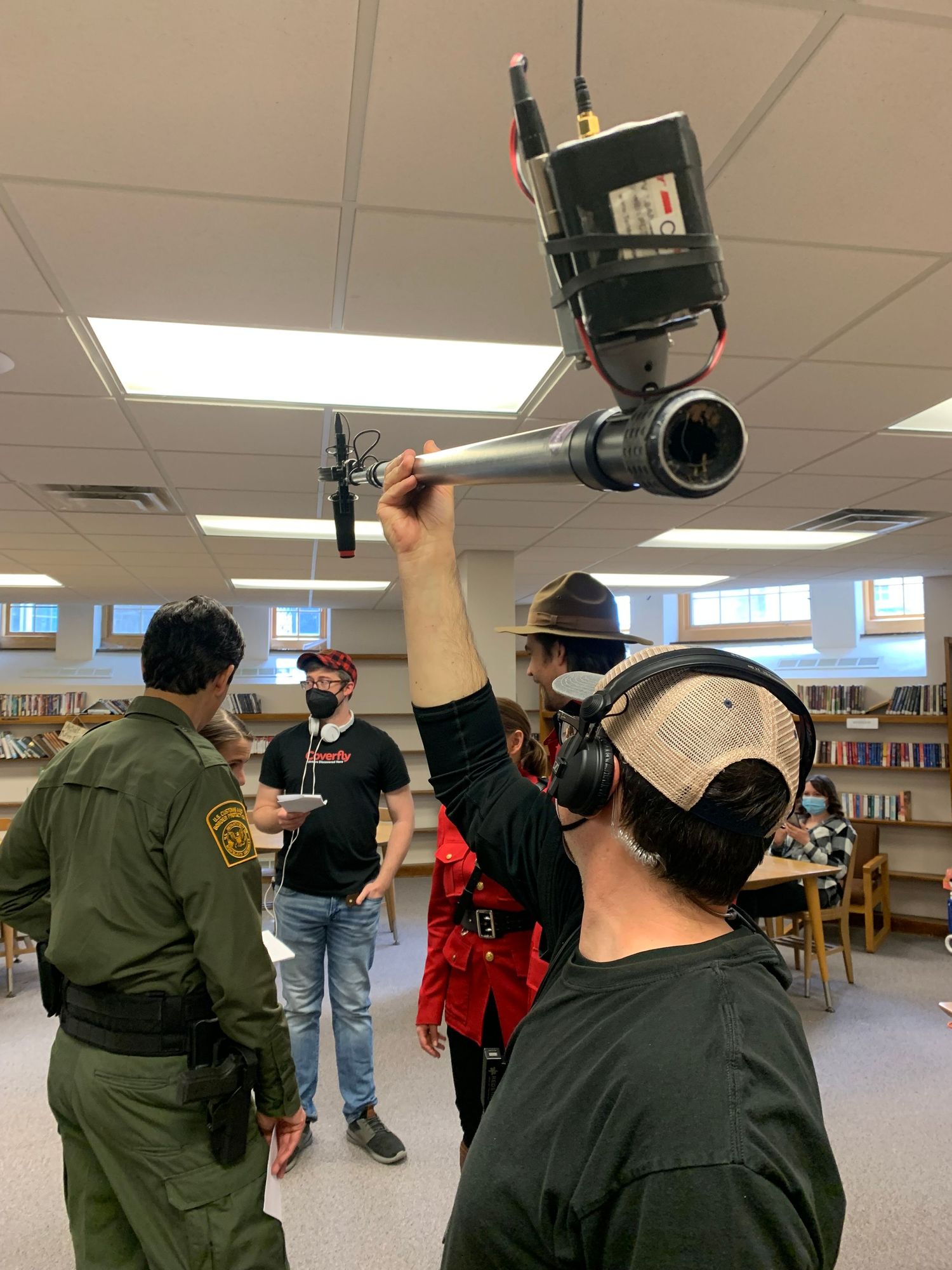 Crew member adjusting camera equipment mounted on ceiling in library setting.