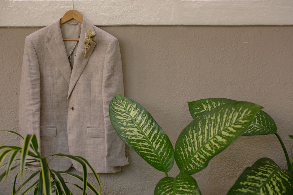 A light gray suit jacket hanging on display with tropical plants in the background.