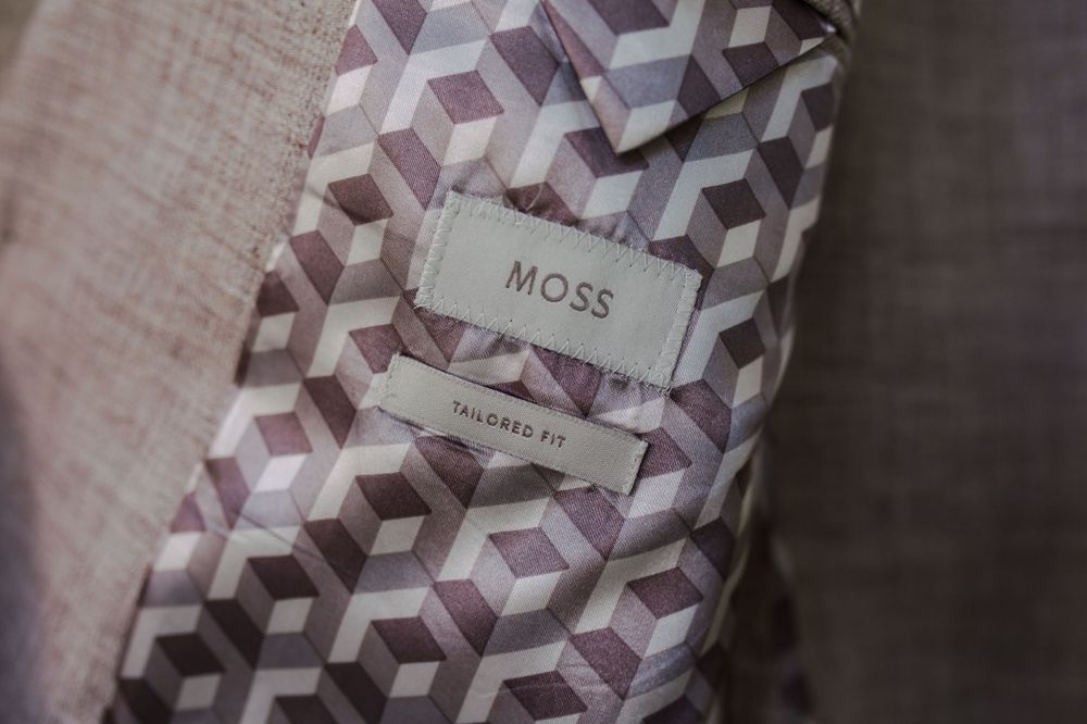 A geometric patterned tie with a label reading 'Moss' against a textured background.