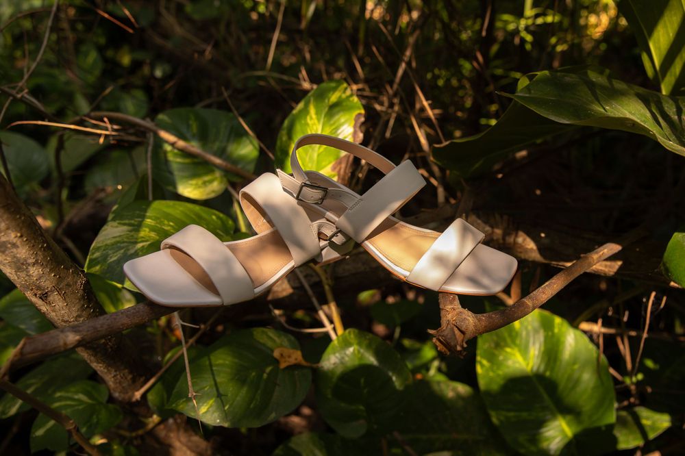 White bridal sandals nestled among green leaves in natural lighting.