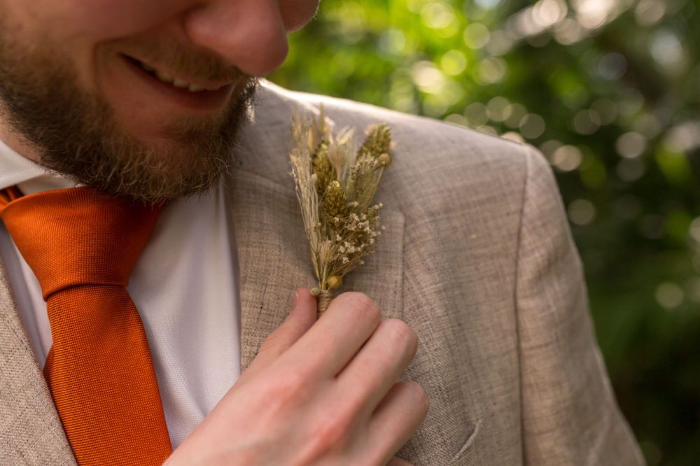 Close-up of dried floral boutonniere pinned to a beige suit jacket with orange tie.