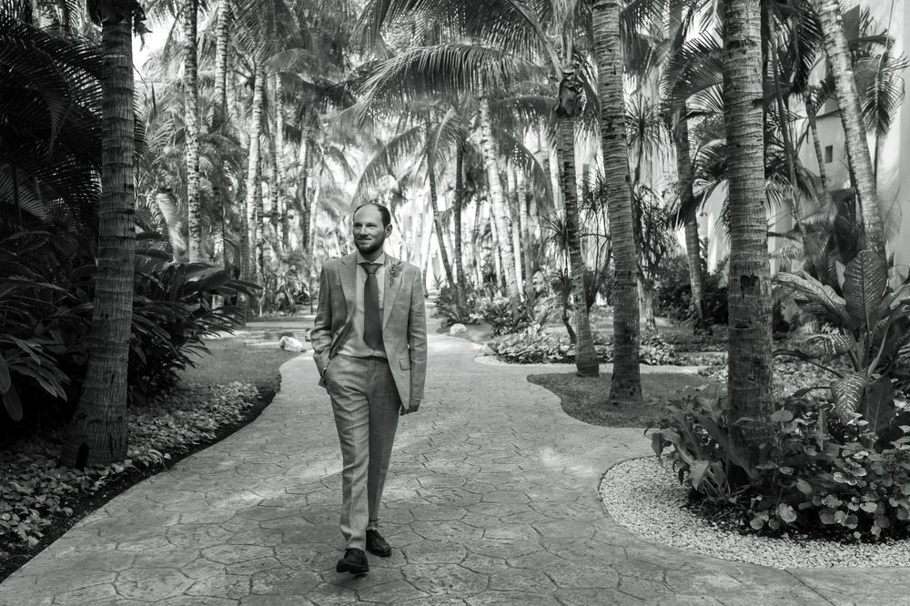 Black and white photo of someone walking down a palm-lined pathway in tropical garden.