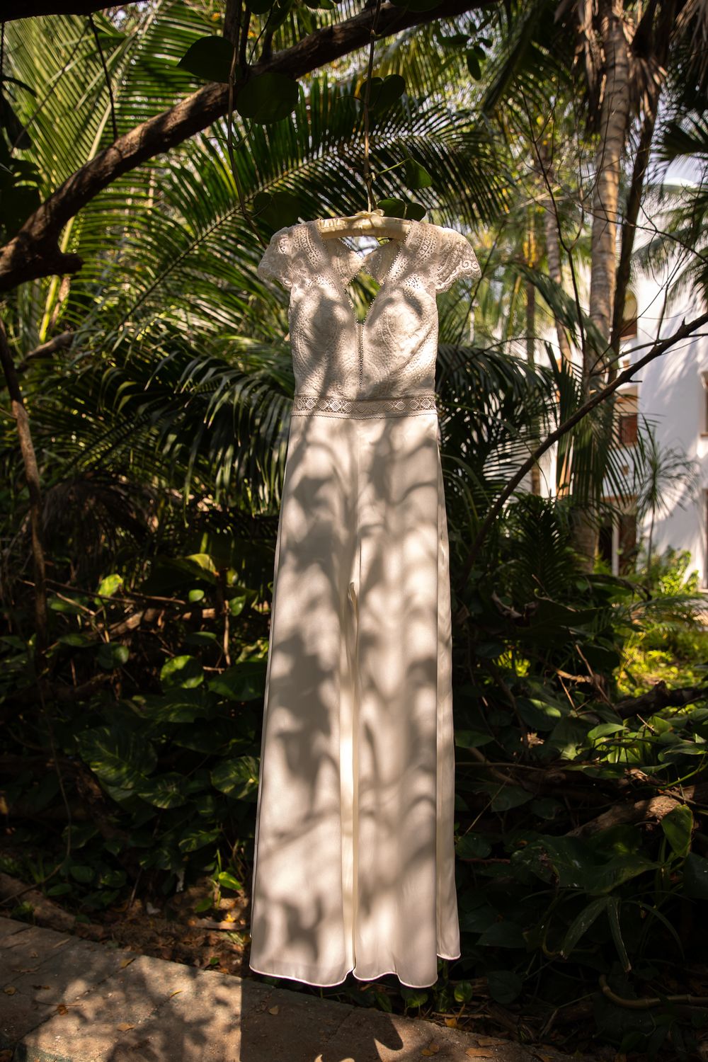 A white wedding dress hanging outdoors against tropical palm fronds and greenery.