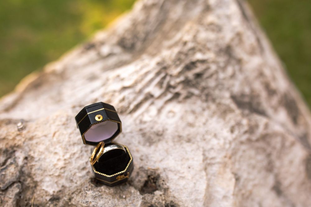 A black ring box opened on a textured stone surface.