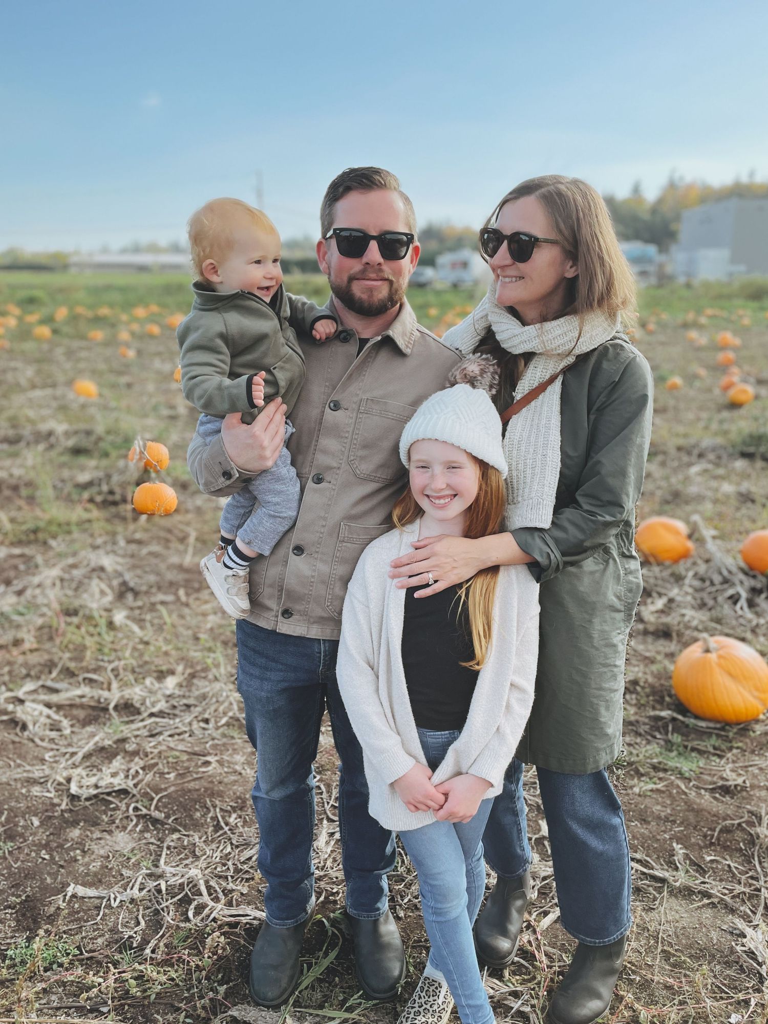 Family poses together at autumn pumpkin patch under clear blue sky.