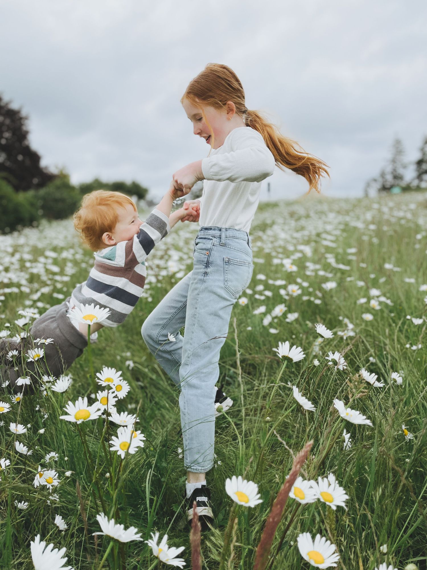 Two children playing and dancing in a field of blooming daisies.