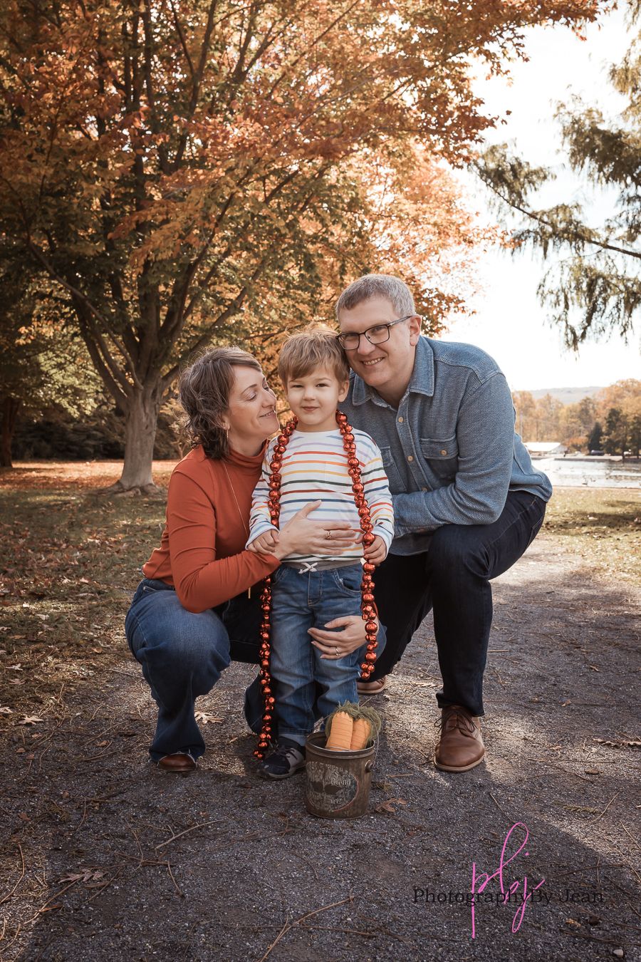 A family shares tender moments together during an autumn photo session under trees with orange-colored leaves.