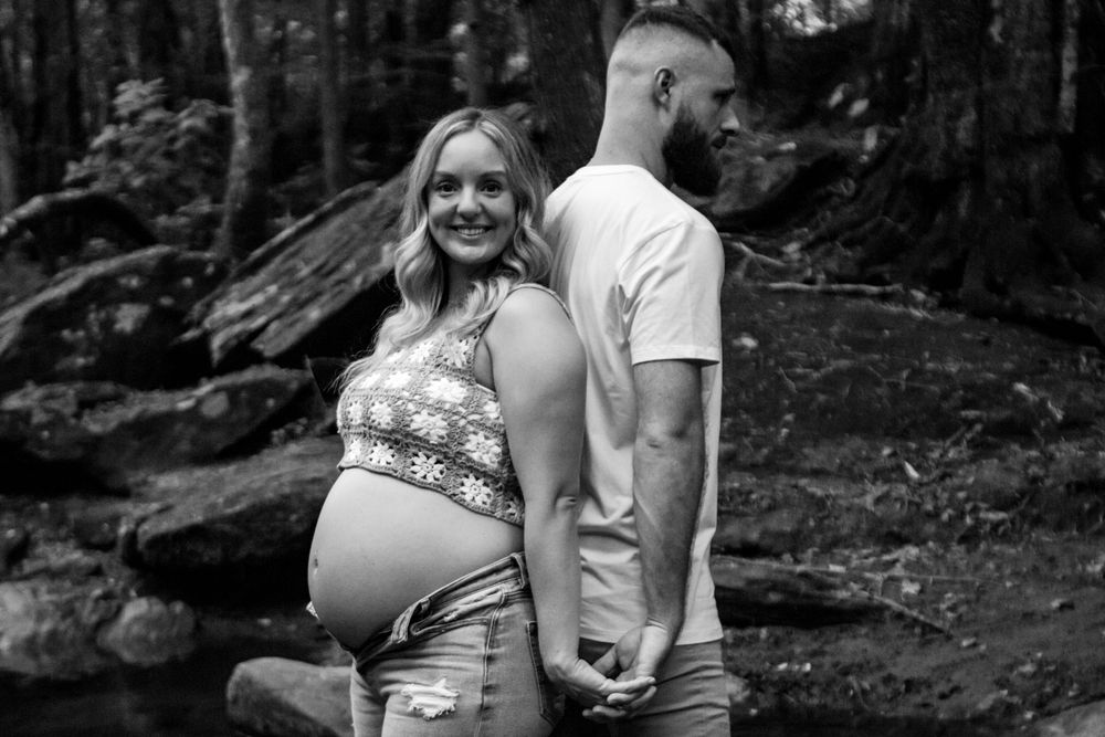 Black and white maternity photos taken in wooded outdoor setting.