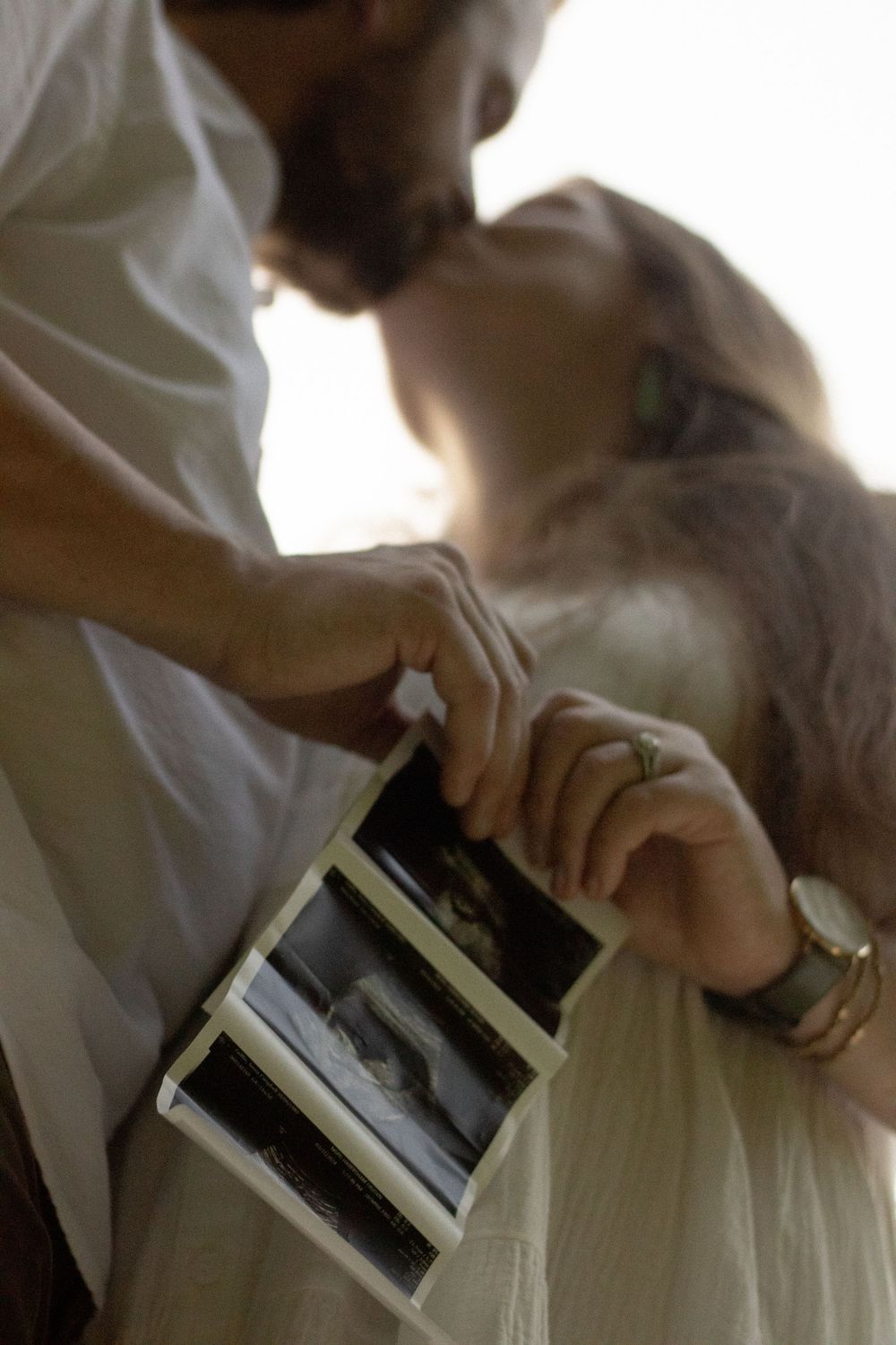 Close-up sequence of hands holding ultrasound photos against white clothing.