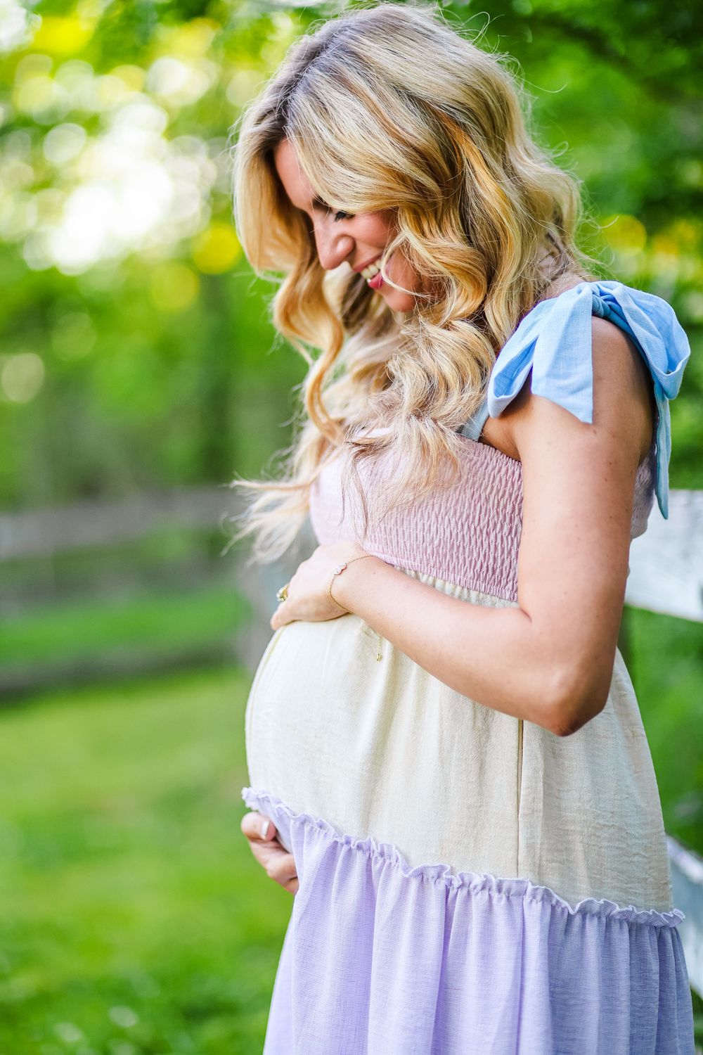 A lifestyle maternity image of a young mother pregnant looking down at her belly and smiling.