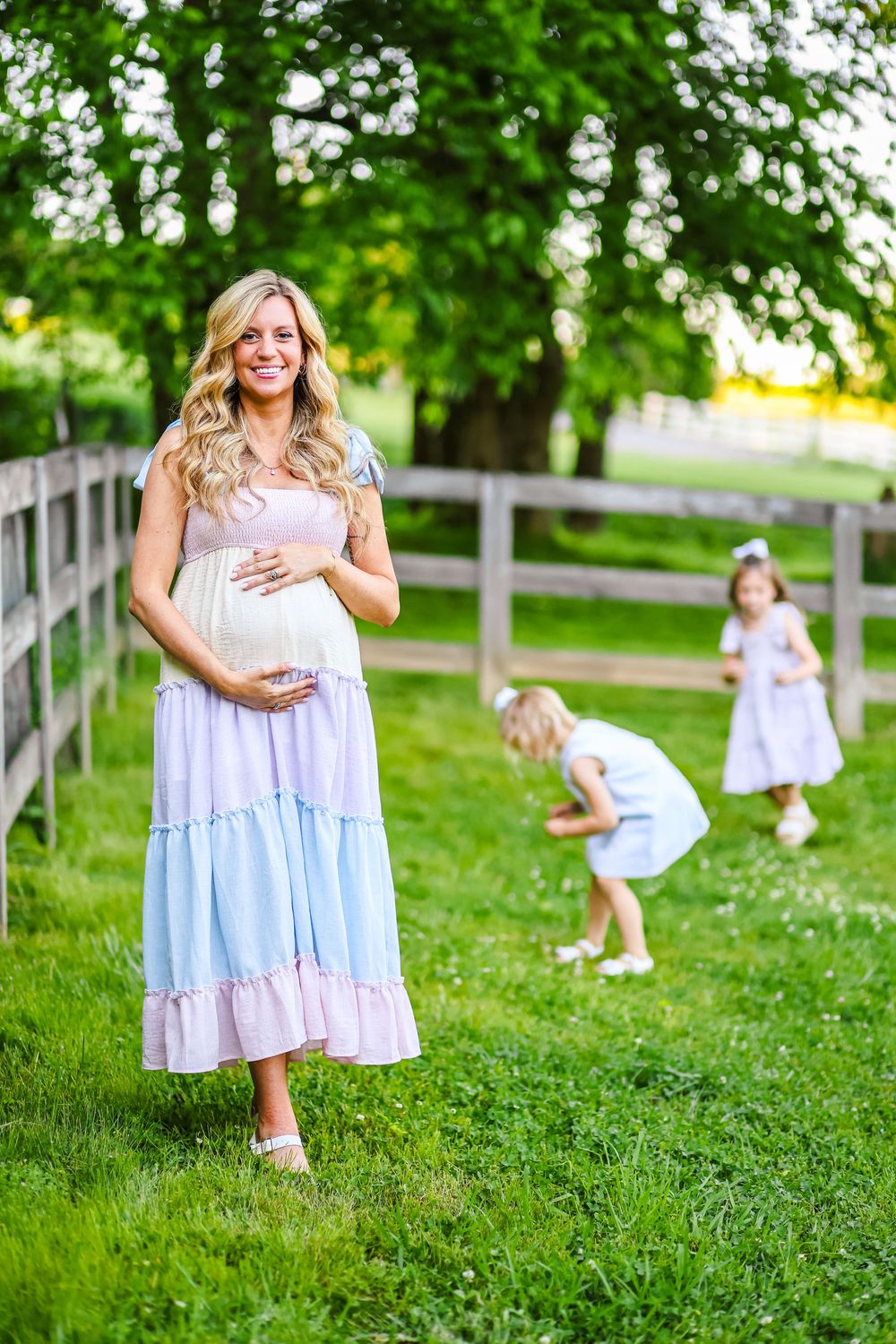 A candid maternity image of a young pregnant mother and her daughters picking flowers in the background.