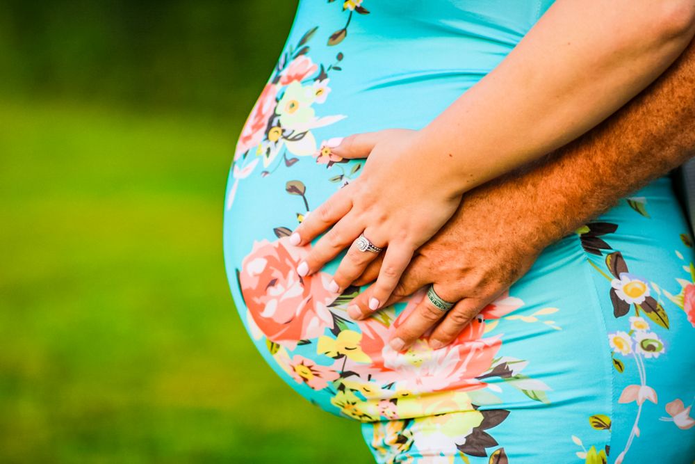 Close-up Maternity photo of a pregnant belly with both parents' ring hands resting over each other.