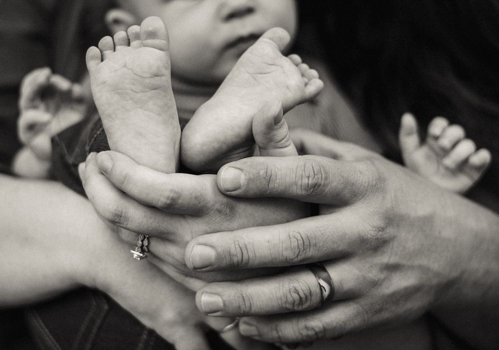 A candid black and white picture of parents holding their baby's feet.