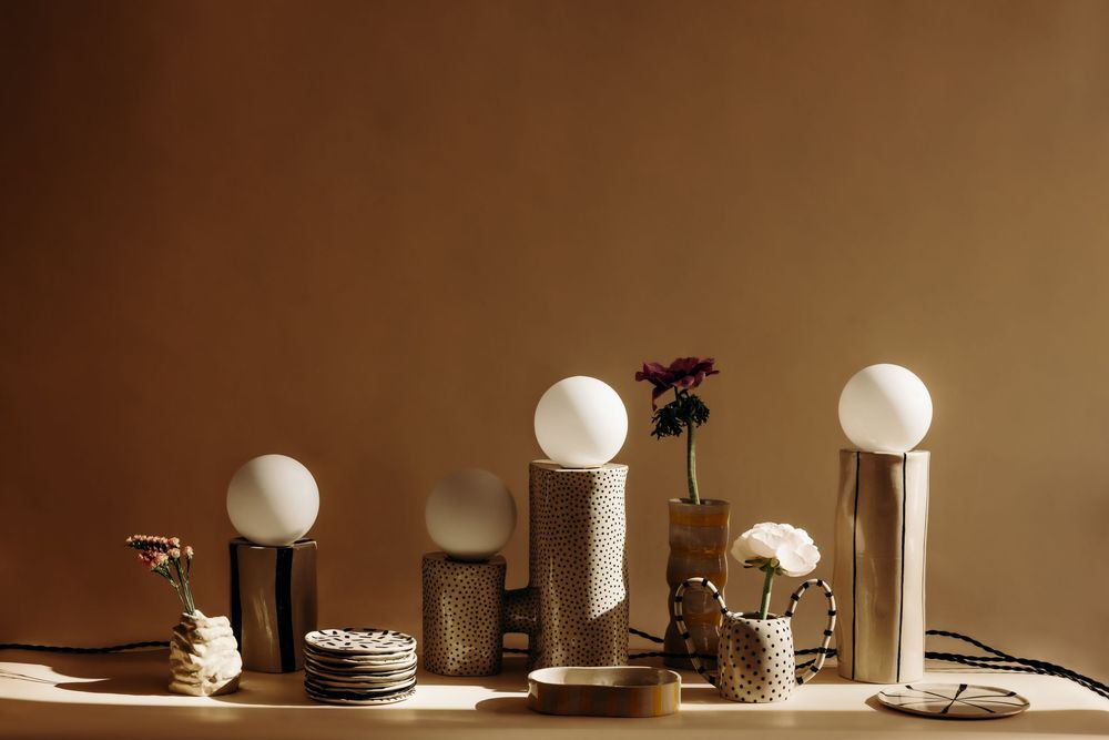 Elegant table lamps with globe bulbs and textured bases displayed on a shelf with small vases against a warm brown wall.