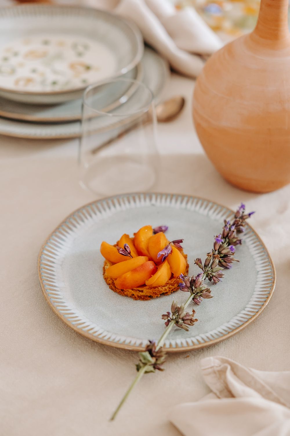 Elegant apricot tart on ceramic plate with lavender sprig, styled on a neutral linen tablescape with terracotta vase.