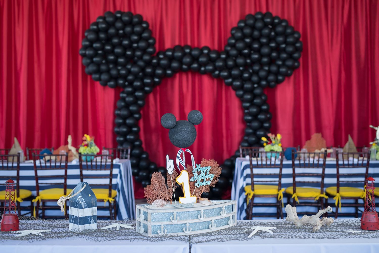 Mickey Mouse themed balloon arch decoration with red curtain backdrop at a Disney Cruise Line themed party celebration.