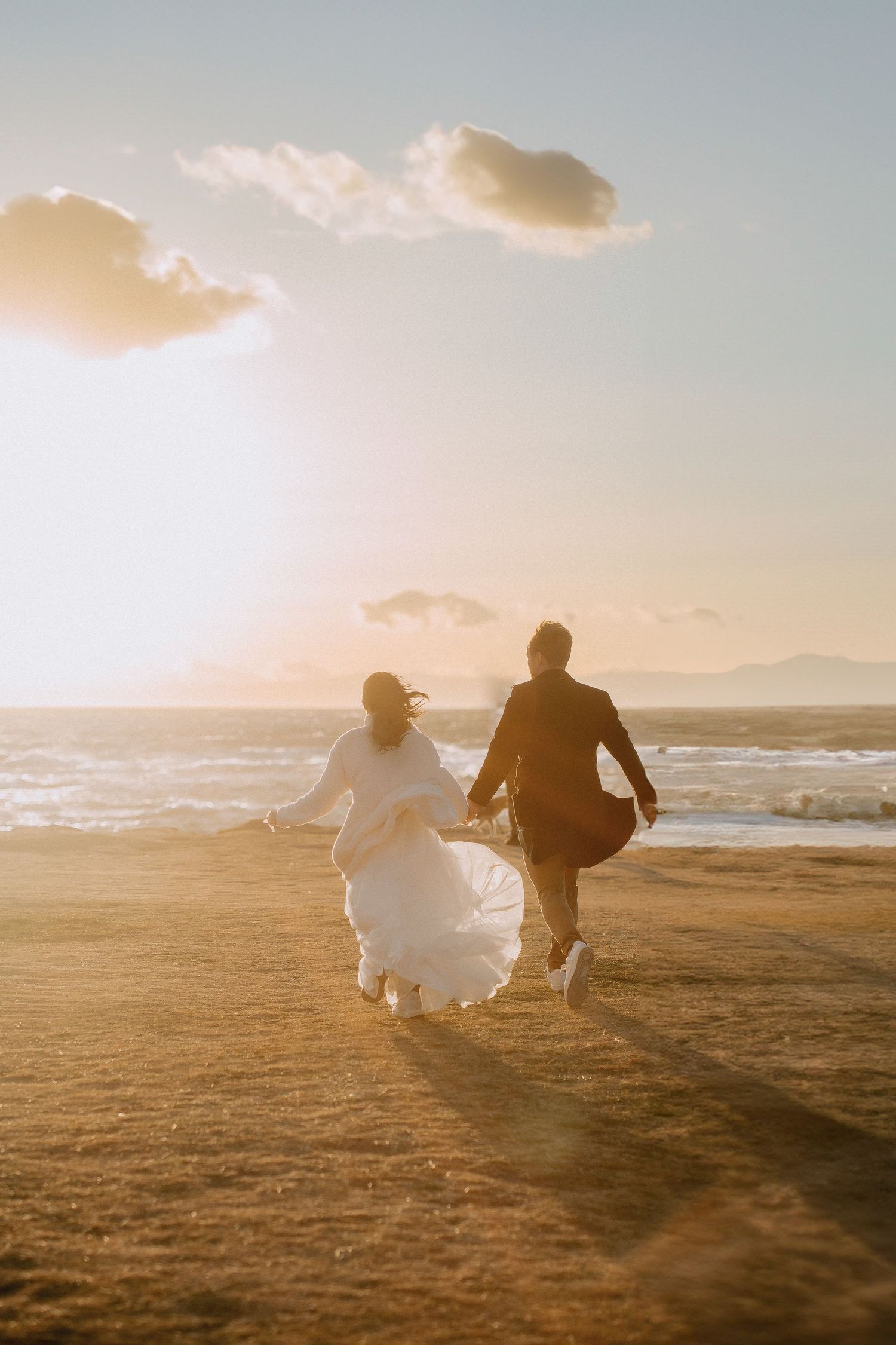 A couple in wedding attire running towards the sunset on a beach in Seattle