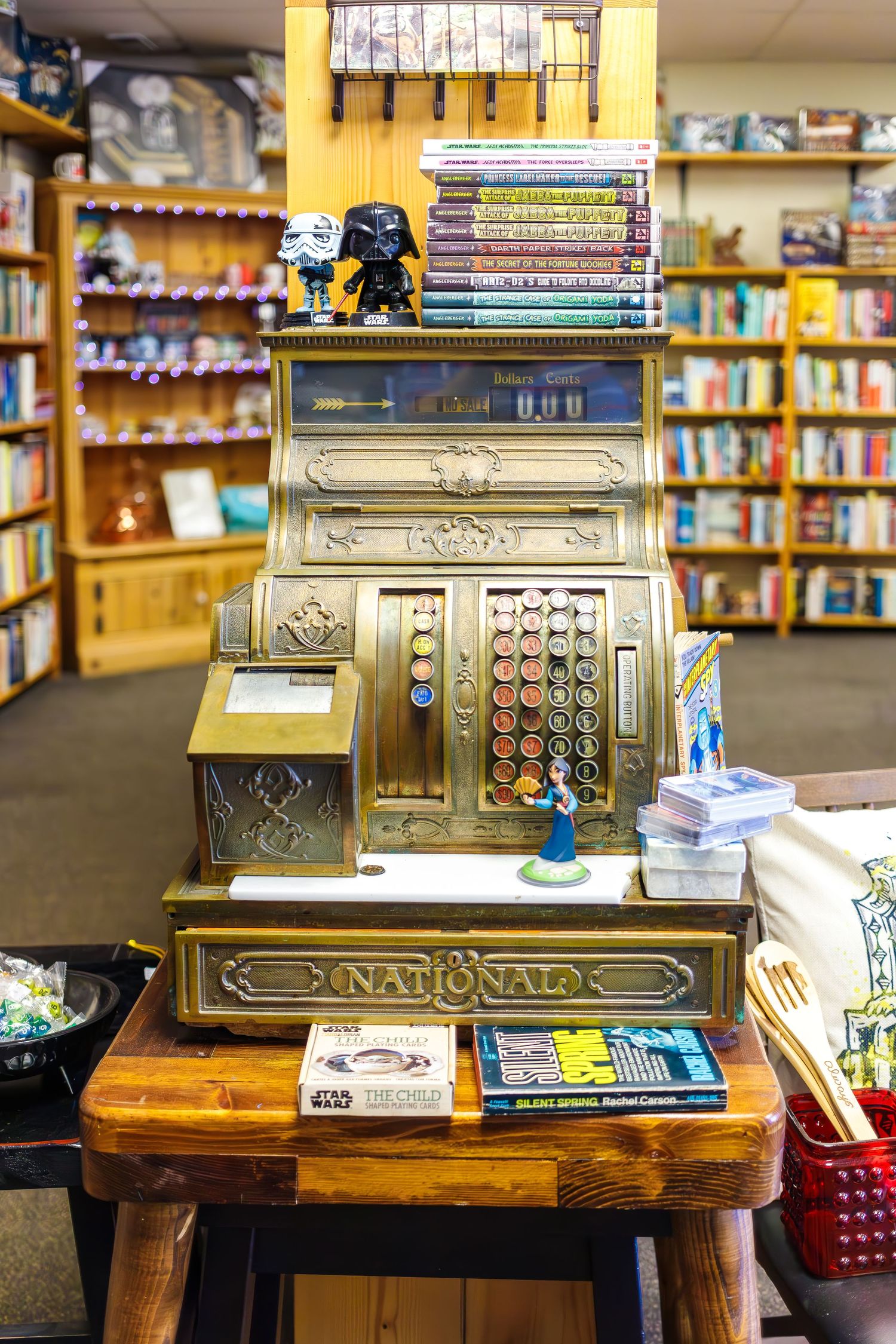 Vintage gold cash register with books and collectibles displayed in bookstore setting.