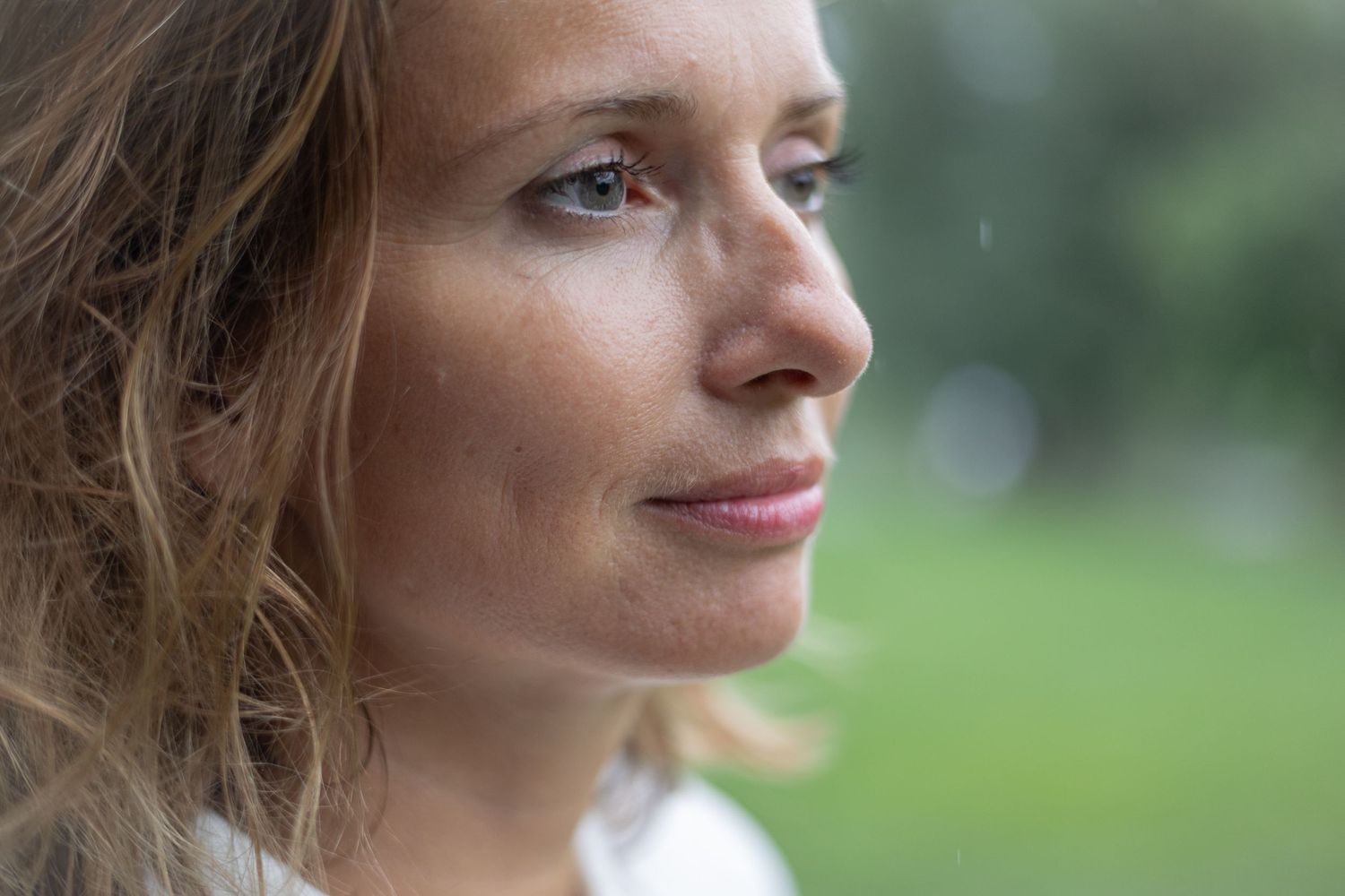 Profile view portrait with soft natural lighting and blurred green background.