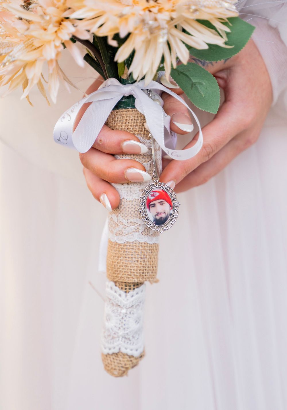Bride holds bouquet with burlap wrap and memorial photo charm honoring loved one at wedding.