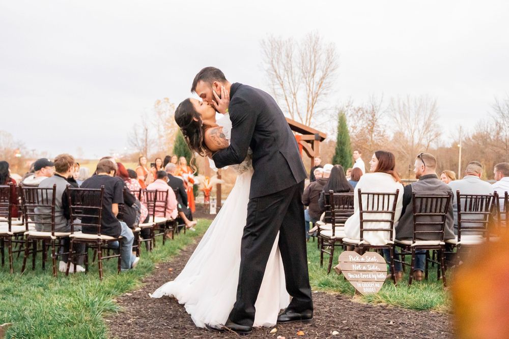Bride and groom share a passionate dip kiss at the end of the outdoor wedding ceremony aisle.