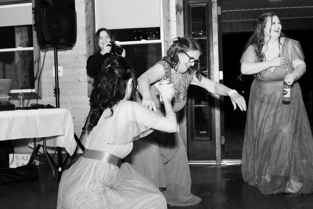 Black and white photo of wedding guests dancing energetically at rustic barn reception.
