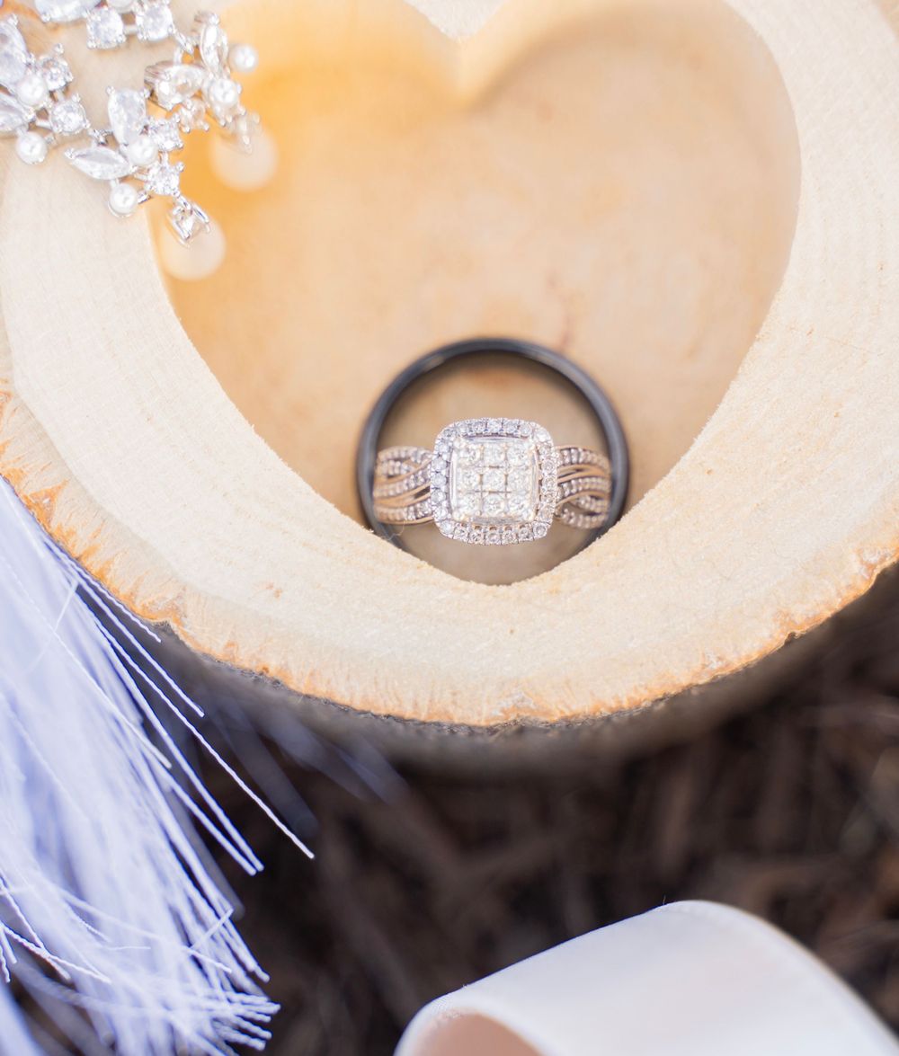Diamond engagement ring and black wedding band displayed in a heart-shaped wood slice.