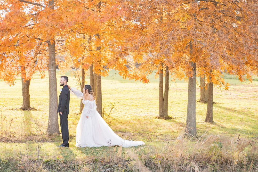 Bride and groom hold hands under vibrant orange fall foliage trees during outdoor wedding photo session.
