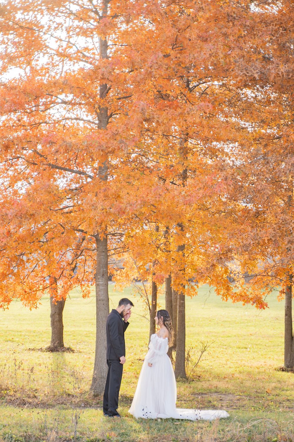 Bride and groom sharing intimate first look moment under stunning orange fall foliage trees outdoors.