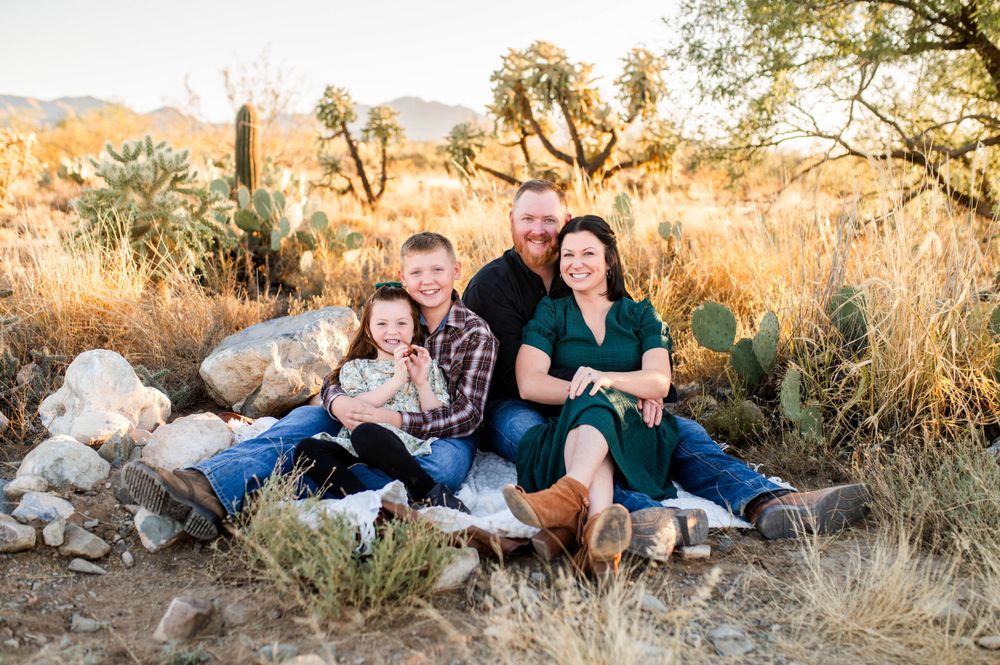 Happy family of four sitting together in a desert landscape with cacti and golden light.