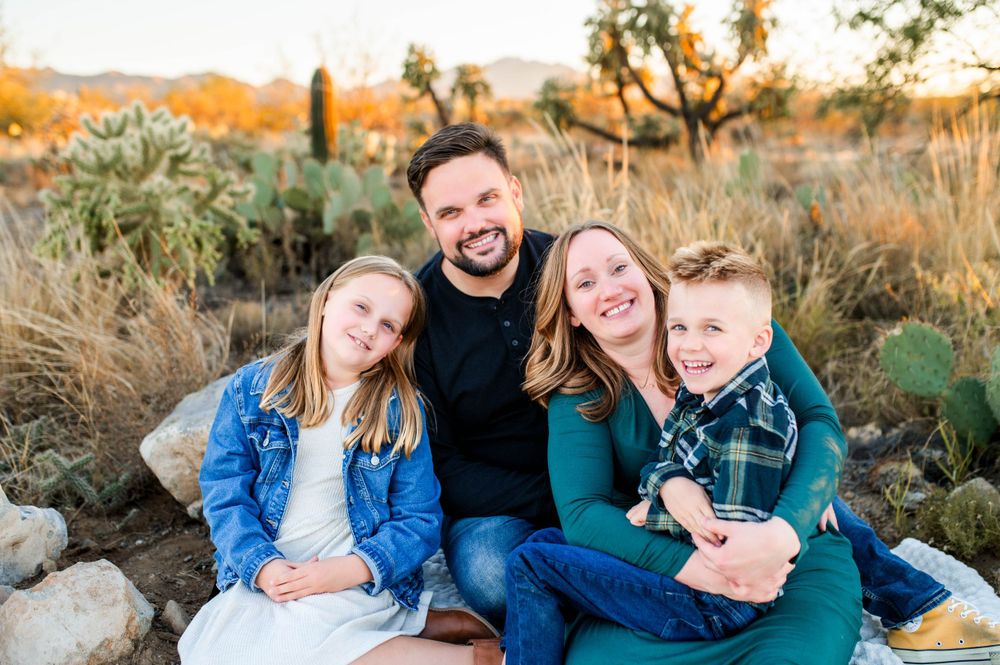 Smiling family of four sitting together in a sunny desert landscape with cacti nearby.