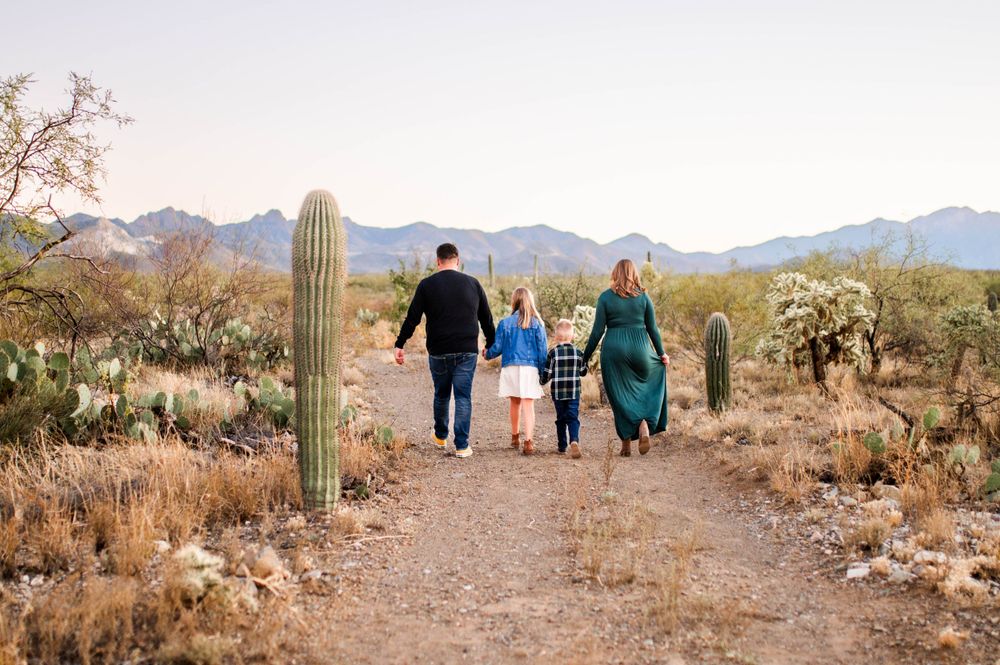 Family of four walking hand in hand down a desert path surrounded by saguaro cacti.