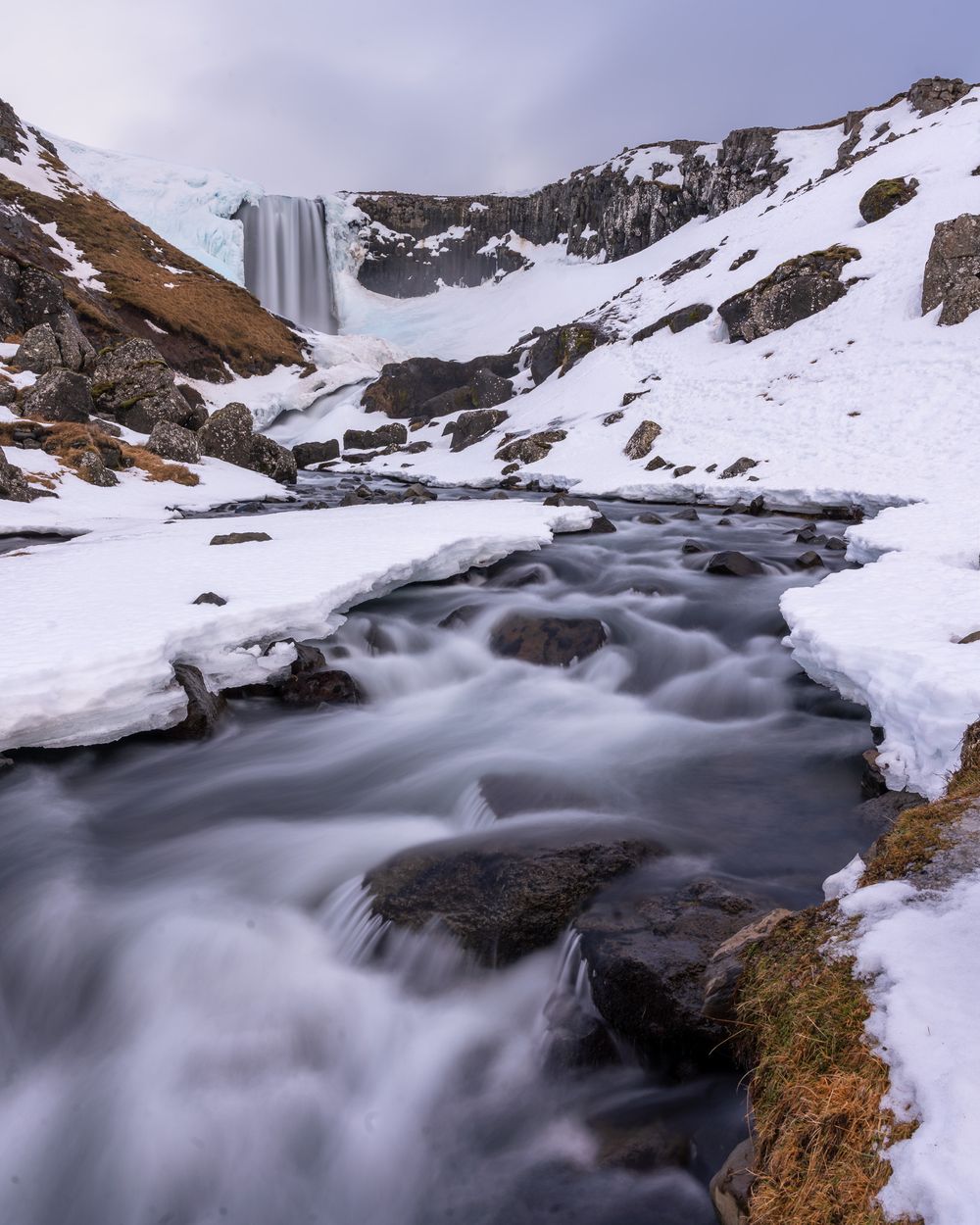 A dramatic Icelandic waterfall cuts through a wintery landscape in this long exposure photograph.