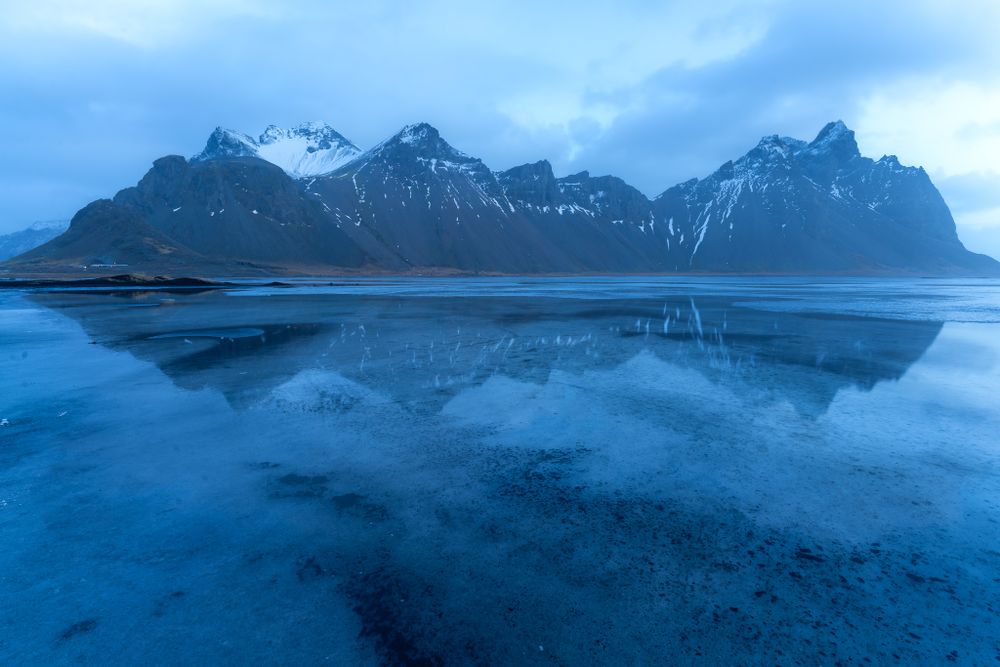 Vestrahorn reflected in the frozen tide at blue hour.