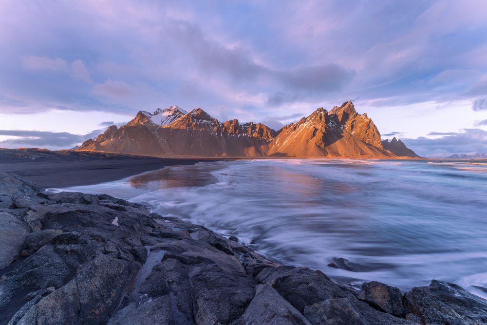 The waning sunlight strikes Vestrahorn as the waves creat a smooth foreground in this long exposure landscape photograph.
