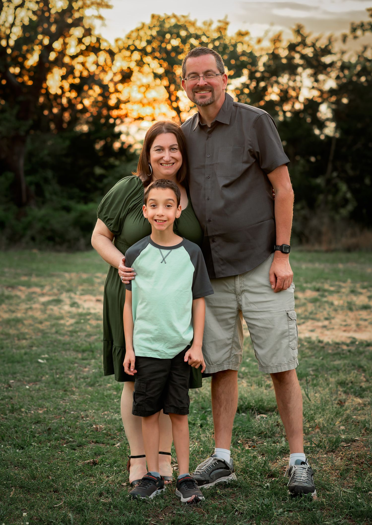 family of 3 with a young son posing at sunset with beautiful bokeh background