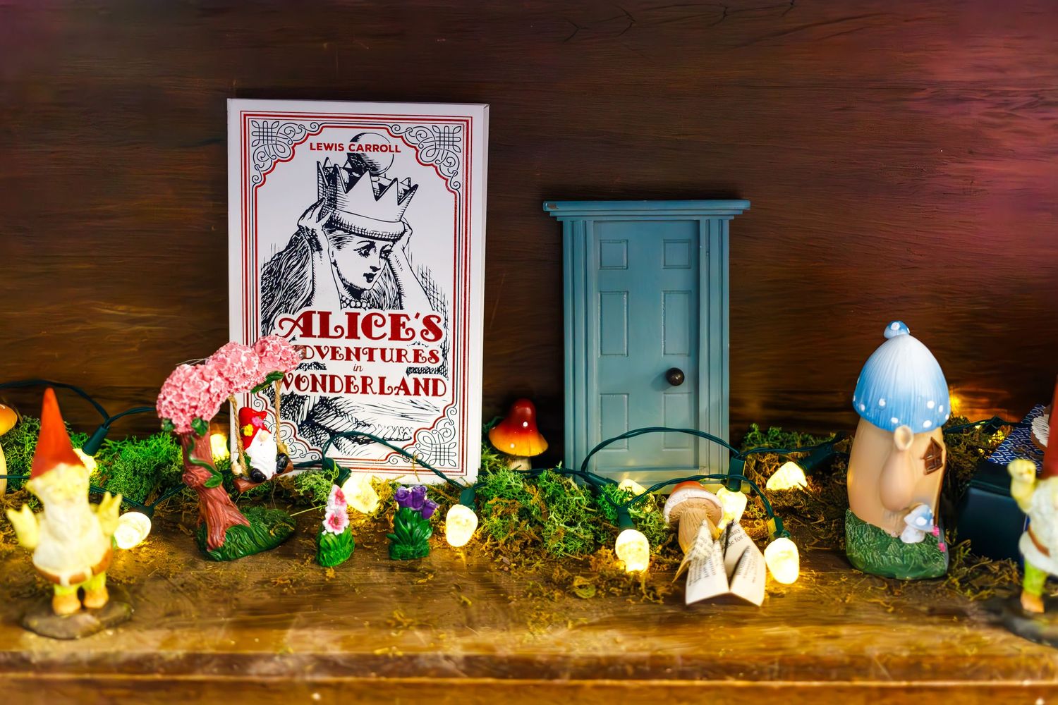 Whimsical Alice in Wonderland themed display with miniature door, book cover, and decorative garden mushrooms.