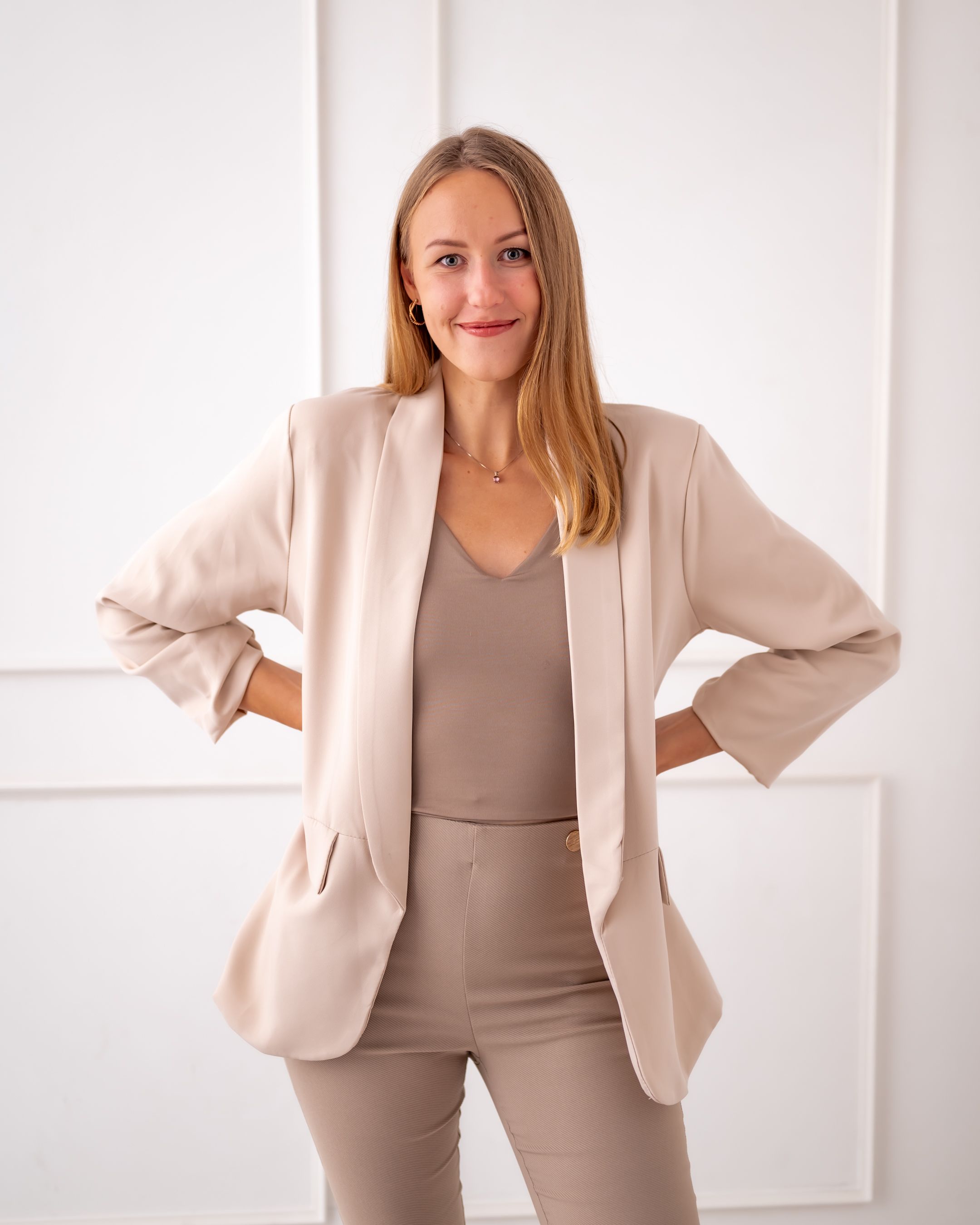 Full body business portrait in cream blazer and taupe pants with hands on hips.