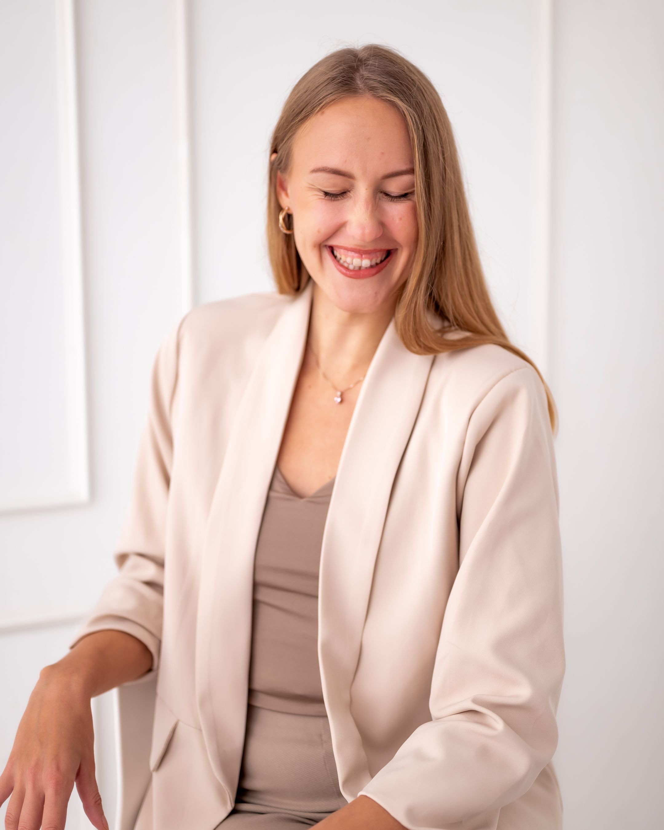 Candid business portrait showing joyful expression in cream colored professional attire.