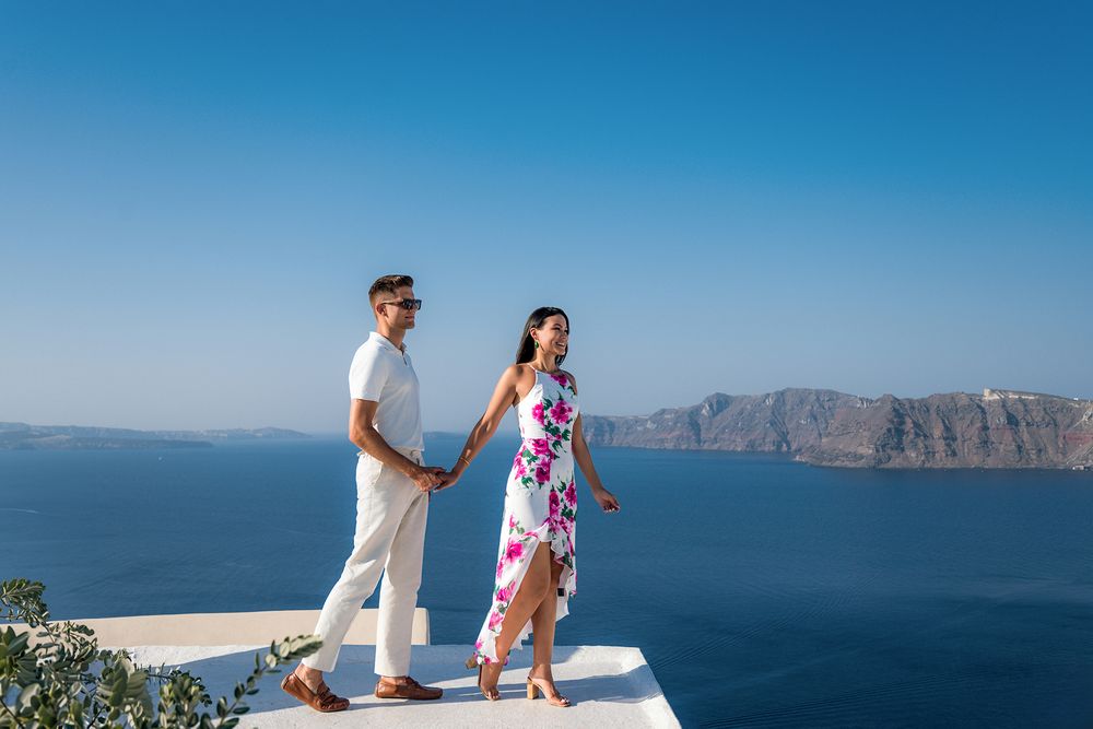 Couple walking on white rooftop terrace with stunning views of Mediterranean coastline and cliffs.